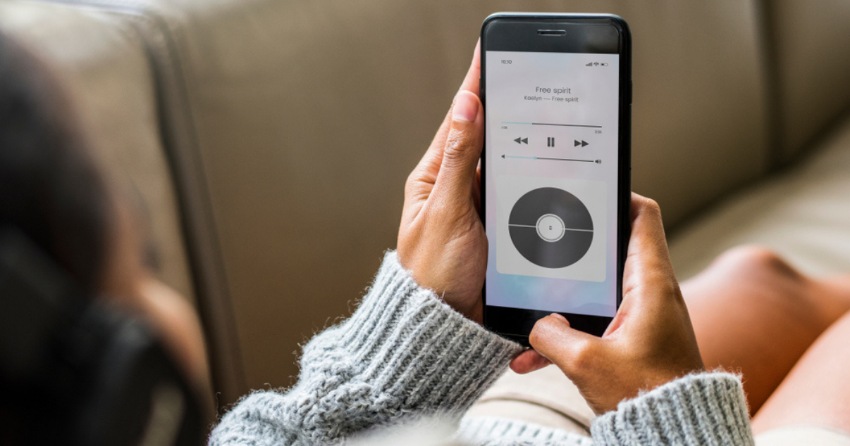 Woman laying on her couch while listening to music she got from a subscription business